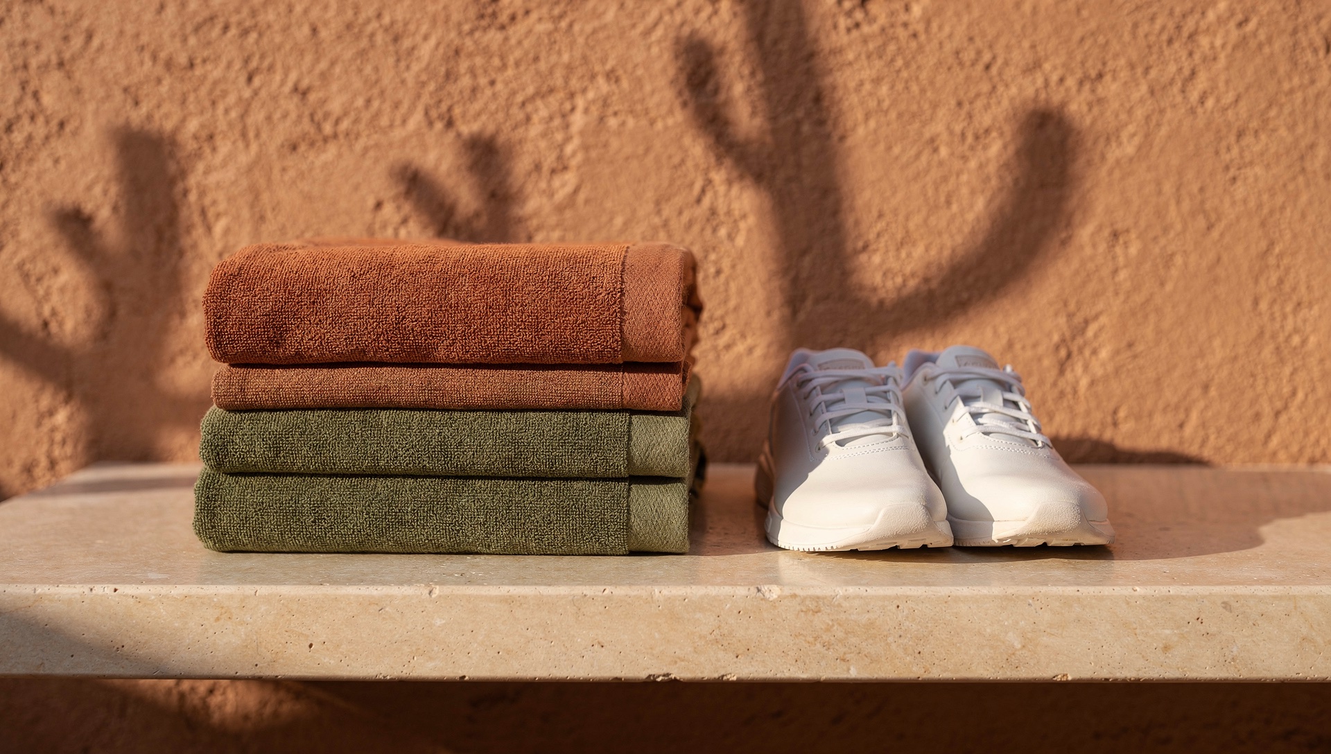 AI illustration of folded terracotta and olive towels beside white athletic shoes.
